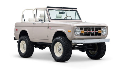 Classic Ford Bronco in dove gray, white wheels, front driver side angle view showing interior seats