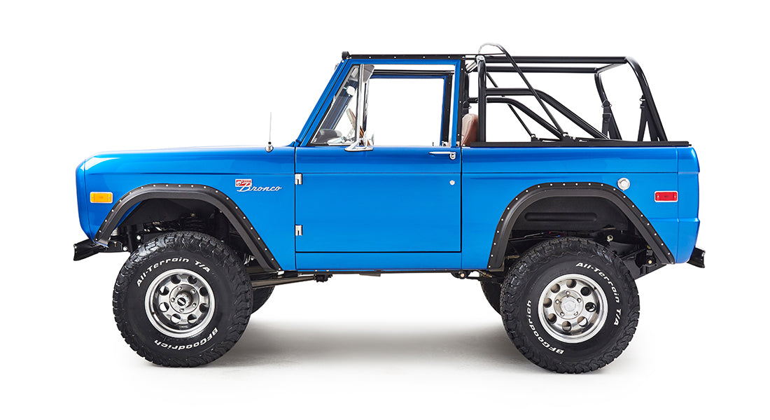 Side view of blue Classic Ford Bronco with black roll cage and off-road tires