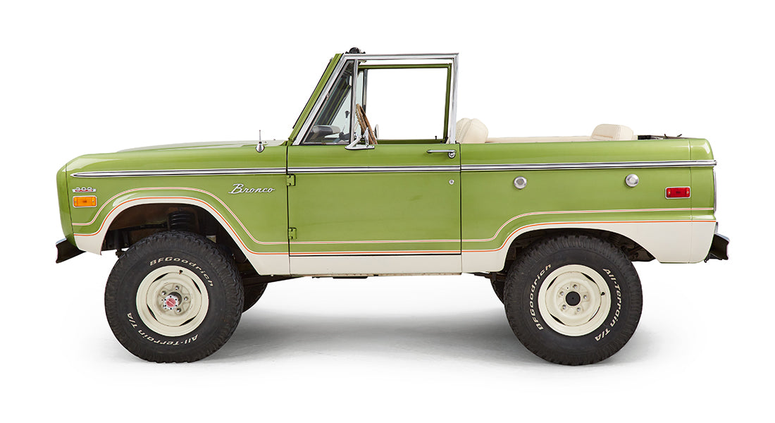 Driver side view of a green Classic Ford Bronco with cream interior and white wheels