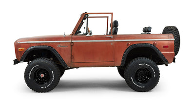 Rust-colored Classic Ford Bronco driver's side view with black wheels and off-road tires.