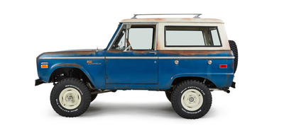 Blue and white Classic Ford Bronco side view with visible rust and off-road tires