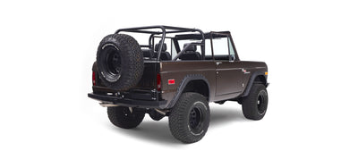 Rear 3/4 view of a brown Classic Ford Bronco with black roll cage and large tires