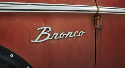 Close-up of 'Bronco' chrome script emblem on rust-colored Classic Ford Bronco.