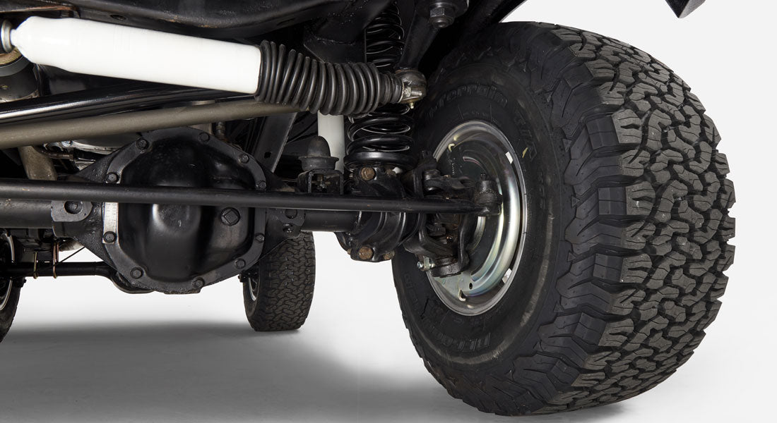 Undercarriage close-up showing wheel assembly, suspension spring, and axle of Classic Ford Bronco