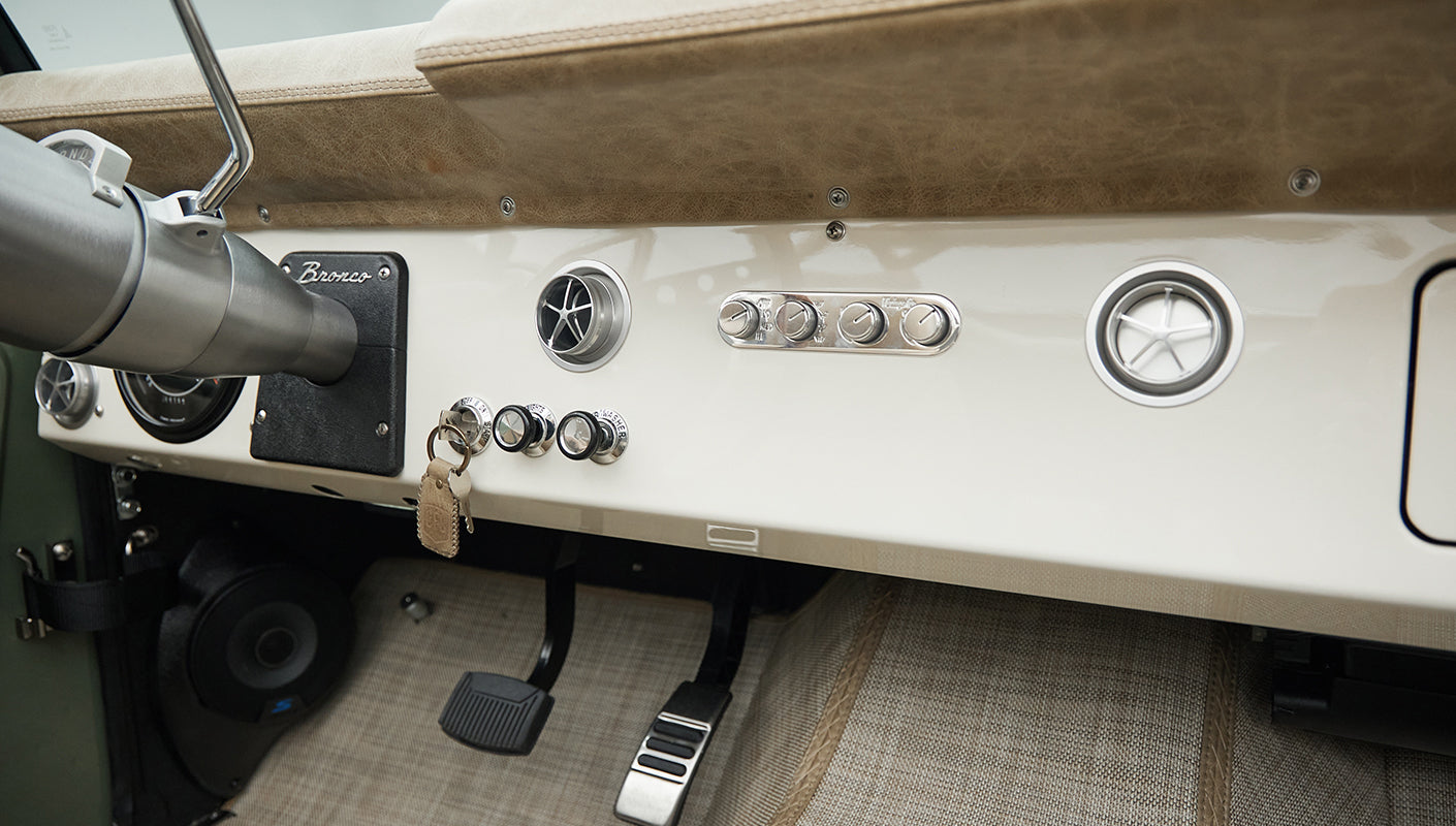 Wide dashboard view of Classic Ford Bronco showing toggle switches and circular vents