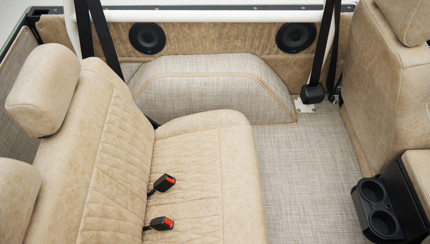 Rear seating area inside Classic Ford Bronco with tan upholstery and seatbelts