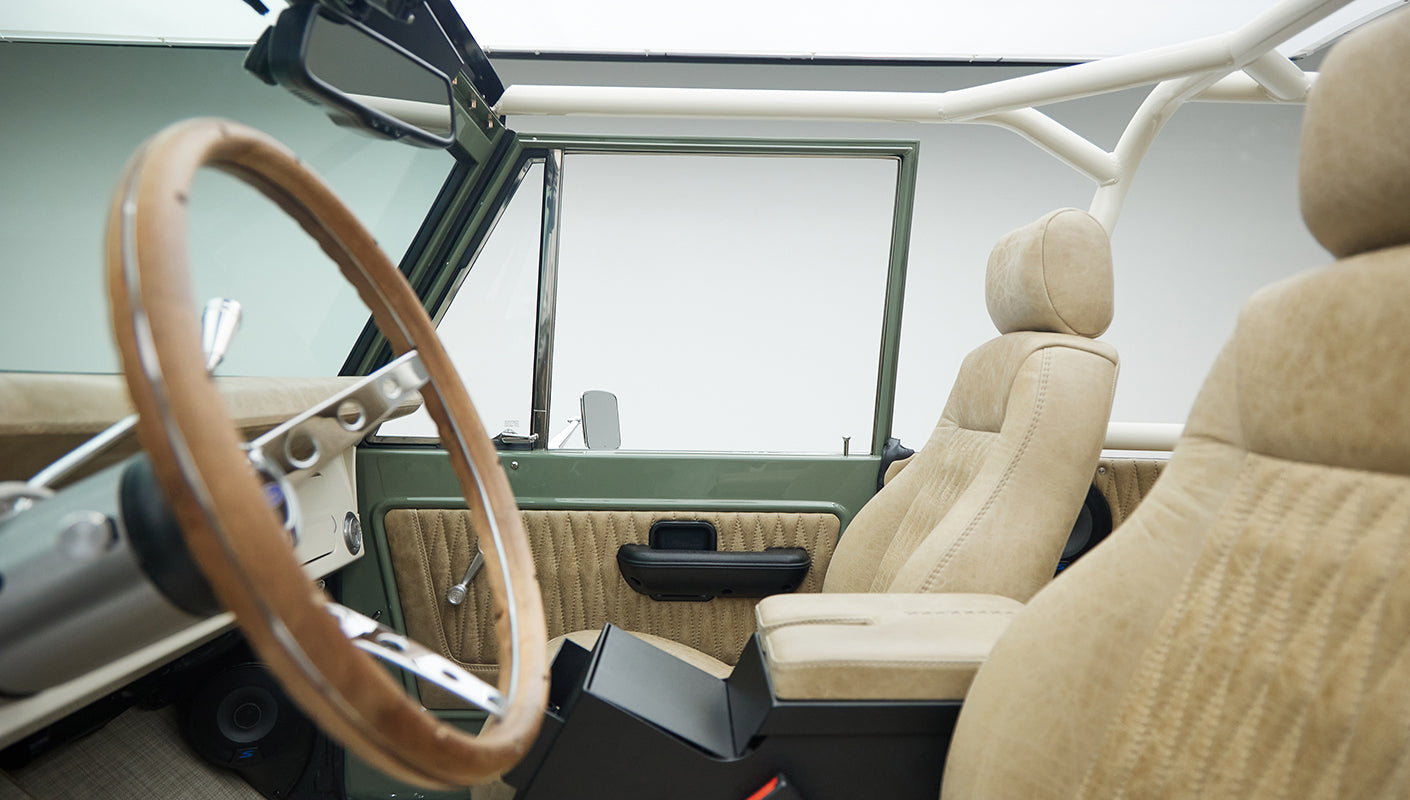 Ford Bronco cabin interior featuring tan quilted leather seats with a wooden steering wheel and roll cage