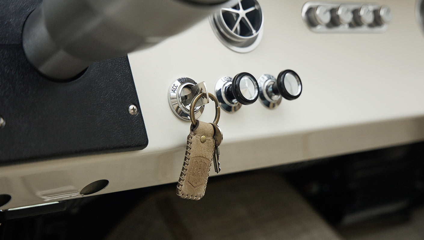 Ignition key with leather key fob inserted in dashboard surrounded by chrome knobs in Classic Ford Bronco