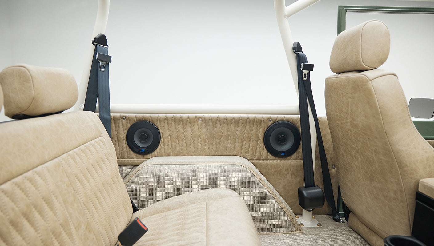 Classic Ford Bronco rear interior with framed roll cage and tan seats with black seat belts