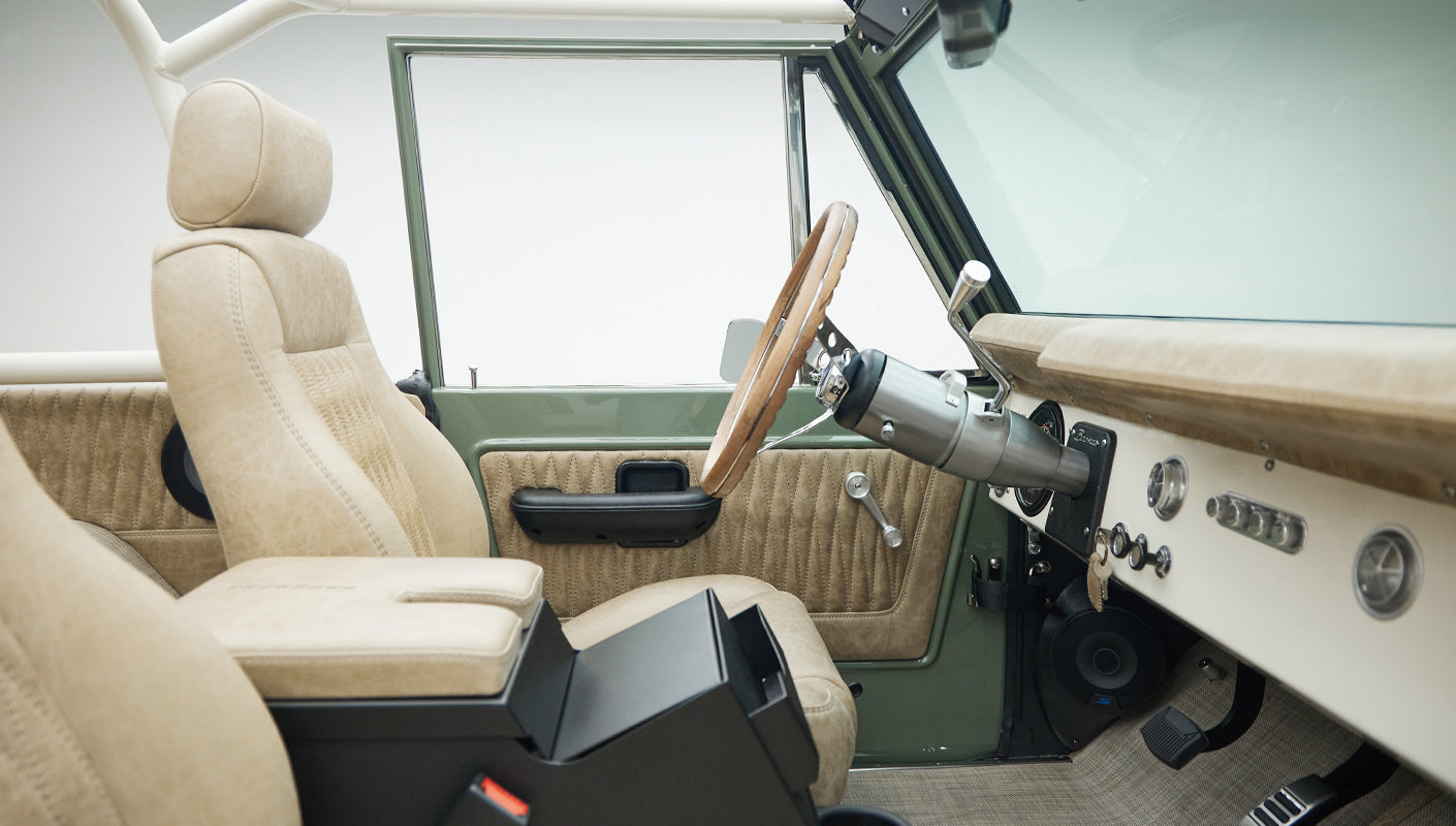 Side view of front interior seats and dashboard of Classic Ford Bronco in tan leather with wooden steering wheel
