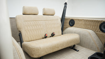 Rear seating area with tan leather bench seat and two speakers mounted on side panels inside Classic Ford Bronco