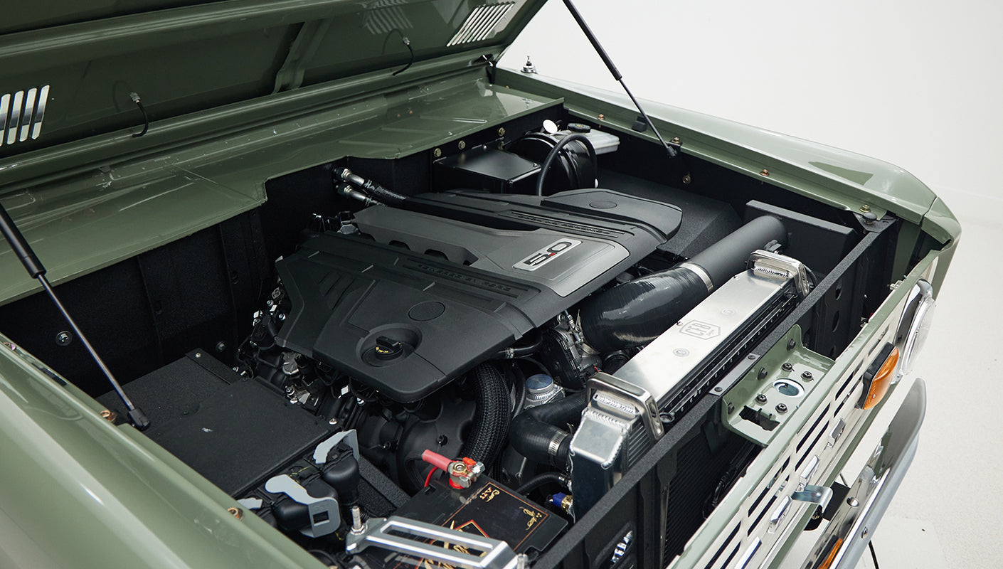 Engine bay of Classic Ford Bronco featuring modern 5.0 liter V8 engine with green exterior paint