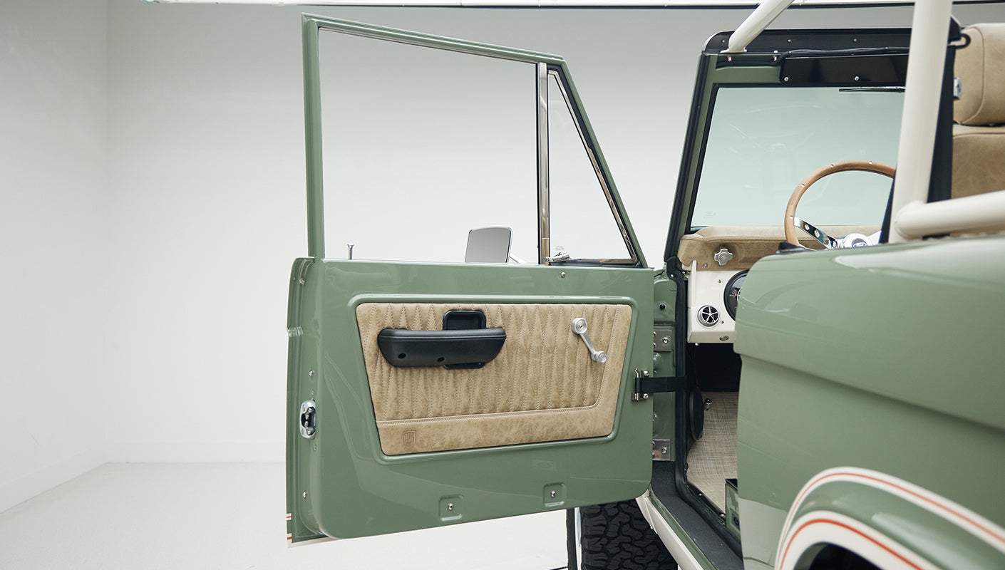 Open driver side door of Classic Ford Bronco with green exterior and tan interior panel