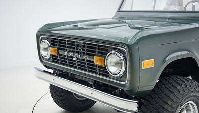Classic Ford Bronco front end in Highland green with chrome bumper and large off-road tires.