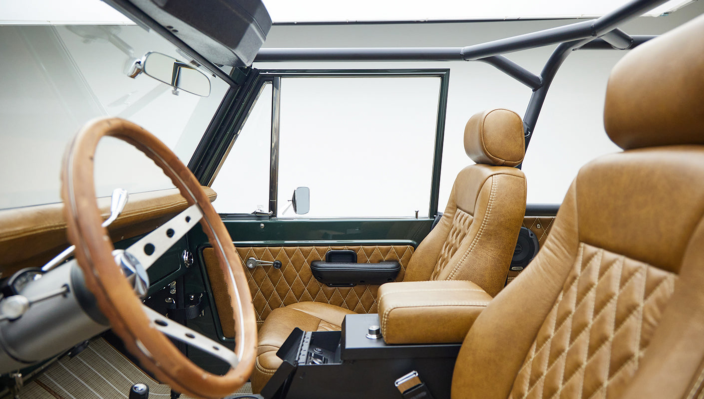 Classic Ford Bronco interior featuring tan quilted leather seats and a wooden steering wheel.