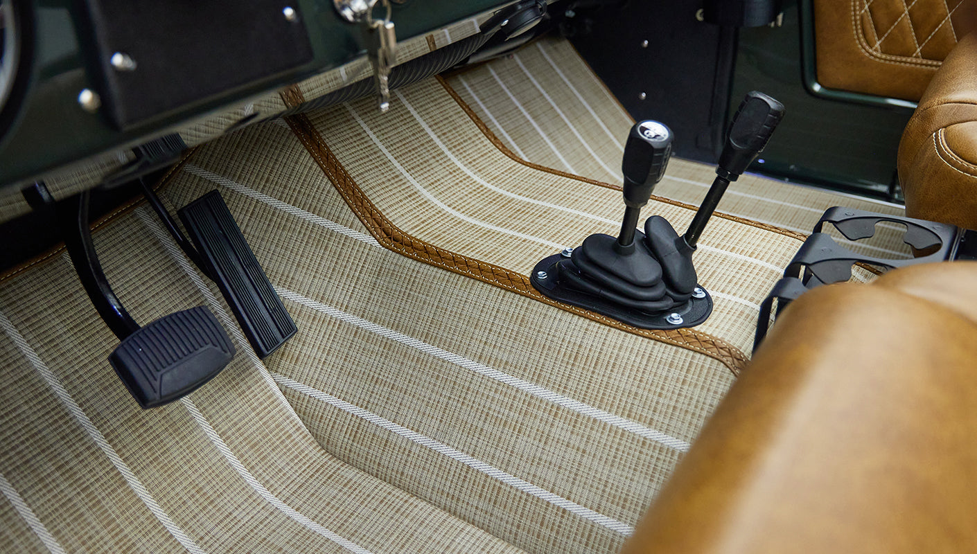 Interior floor area of a vehicle with two gear shifts, brown leather seats, and striped floor mat.