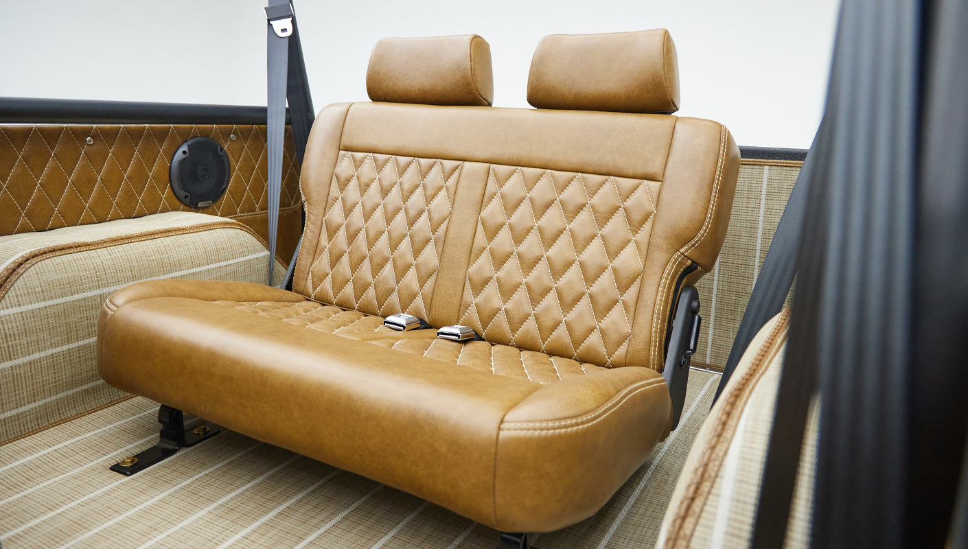 Rear bench seat upholstered in tan diamond-stitched leather with matching interior panels and seat belts.