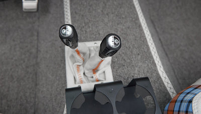 Console with two black gear shift knobs with white leather covers and orange stitching on gray carpet floor