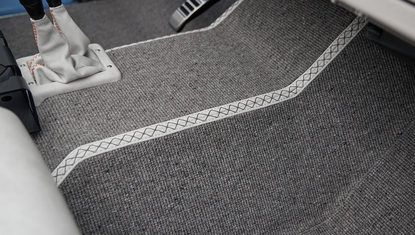 Gray carpeted floor with white leather trim and orange stitching around gear shift area inside Classic Ford Bronco