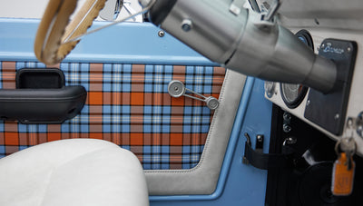 Detailed view of blue and orange plaid door panel, black lock, and white leather seat inside Classic Ford Bronco