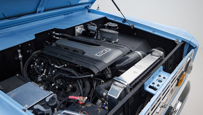 Blue Classic Ford Bronco with hood open showing a modern 5.0 engine in engine bay