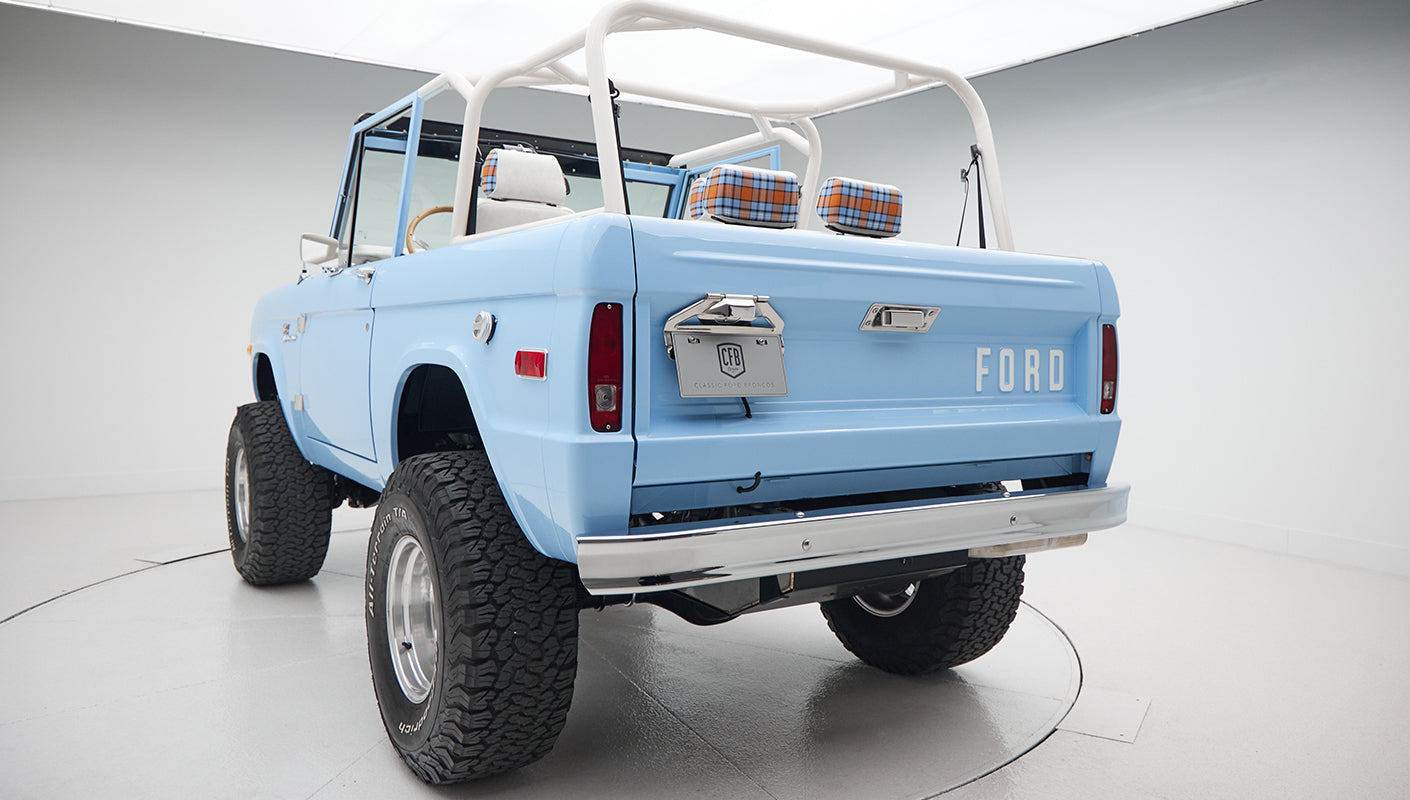 Full rear view of Wind Blue Classic Ford Bronco with lifted tires and plaid interior headrests