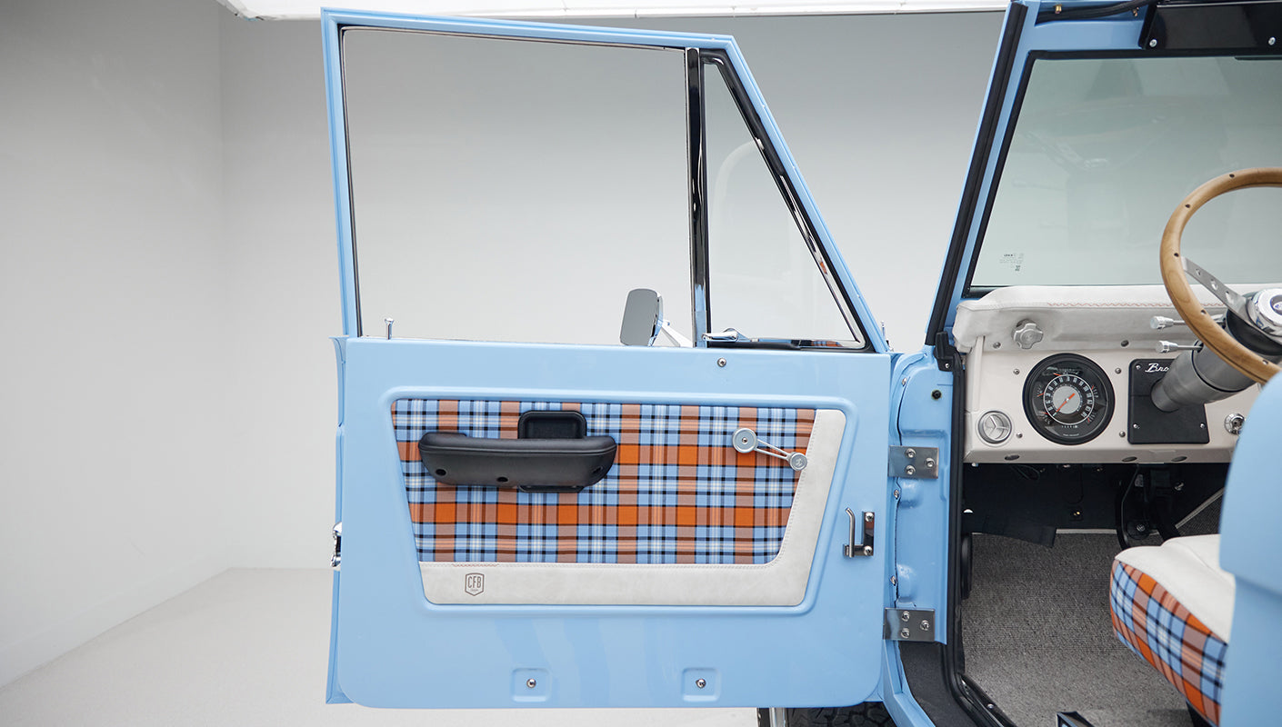 Open driver-side door of Classic Ford Bronco showing blue and orange plaid interior panel