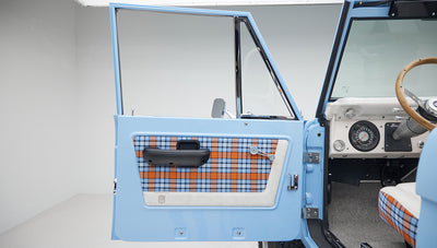 Open driver-side door of Classic Ford Bronco showing blue and orange plaid interior panel