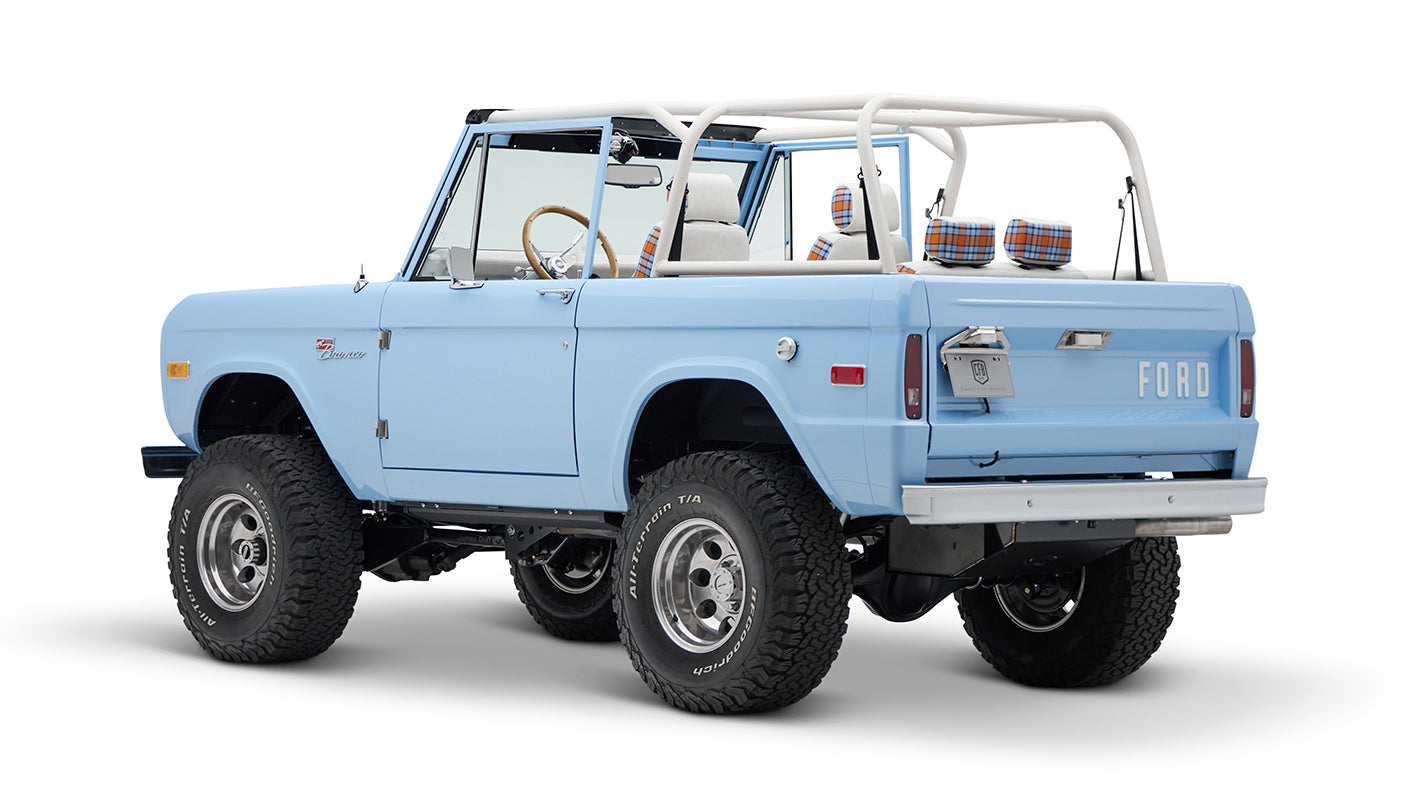 Classic Ford Bronco light blue rear three-quarter view with white roll bar and plaid seat headrests