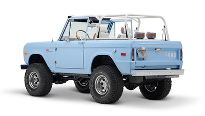 Classic Ford Bronco light blue rear three-quarter view with white roll bar and plaid seat headrests