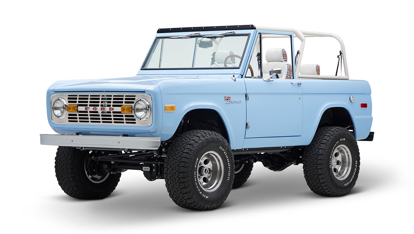 Light blue Classic Ford Bronco with beige roll cage and plaid seats, angled front view