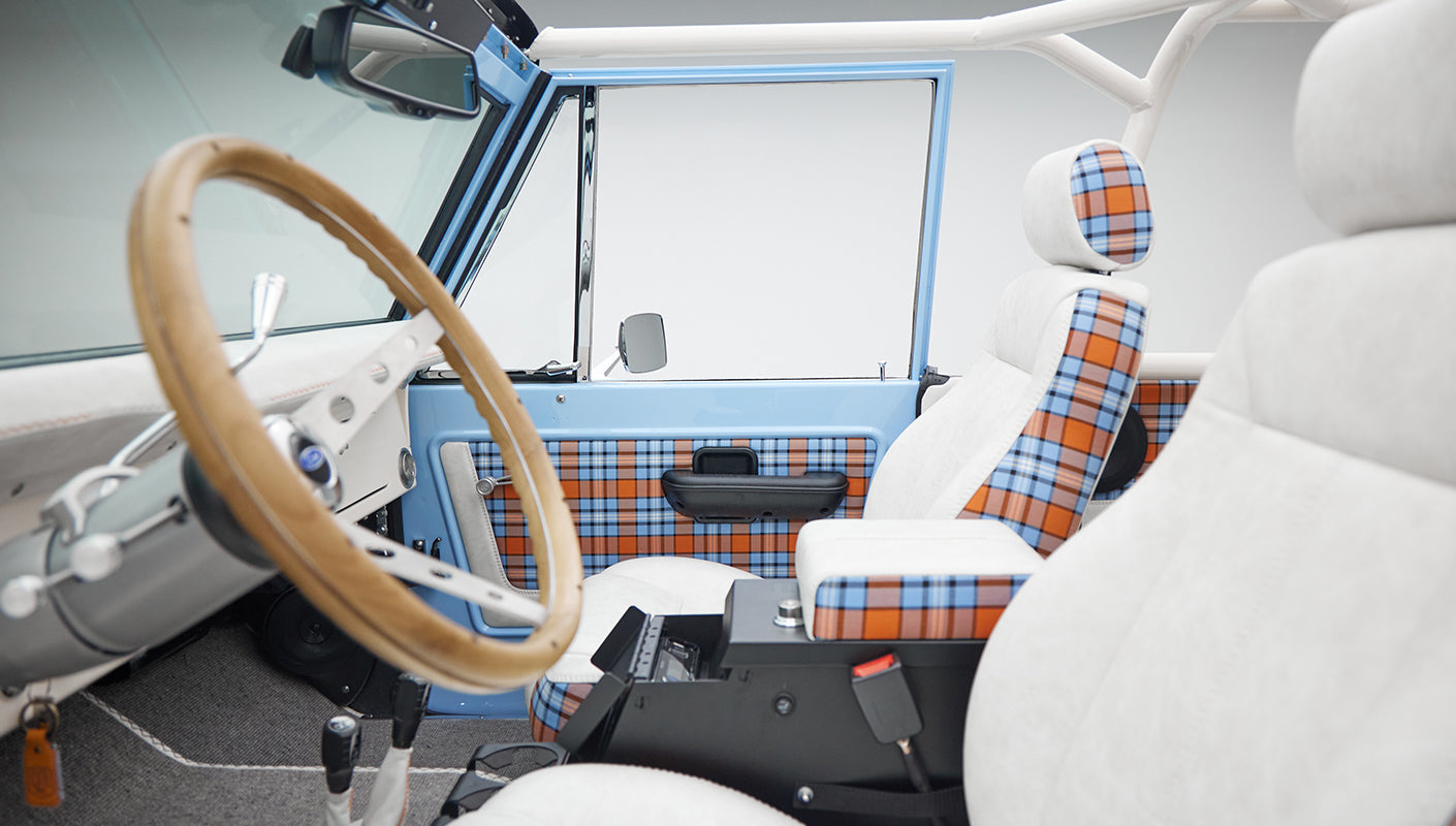 Driver and passenger seats of Classic Ford Bronco with white and plaid upholstery and wooden steering wheel