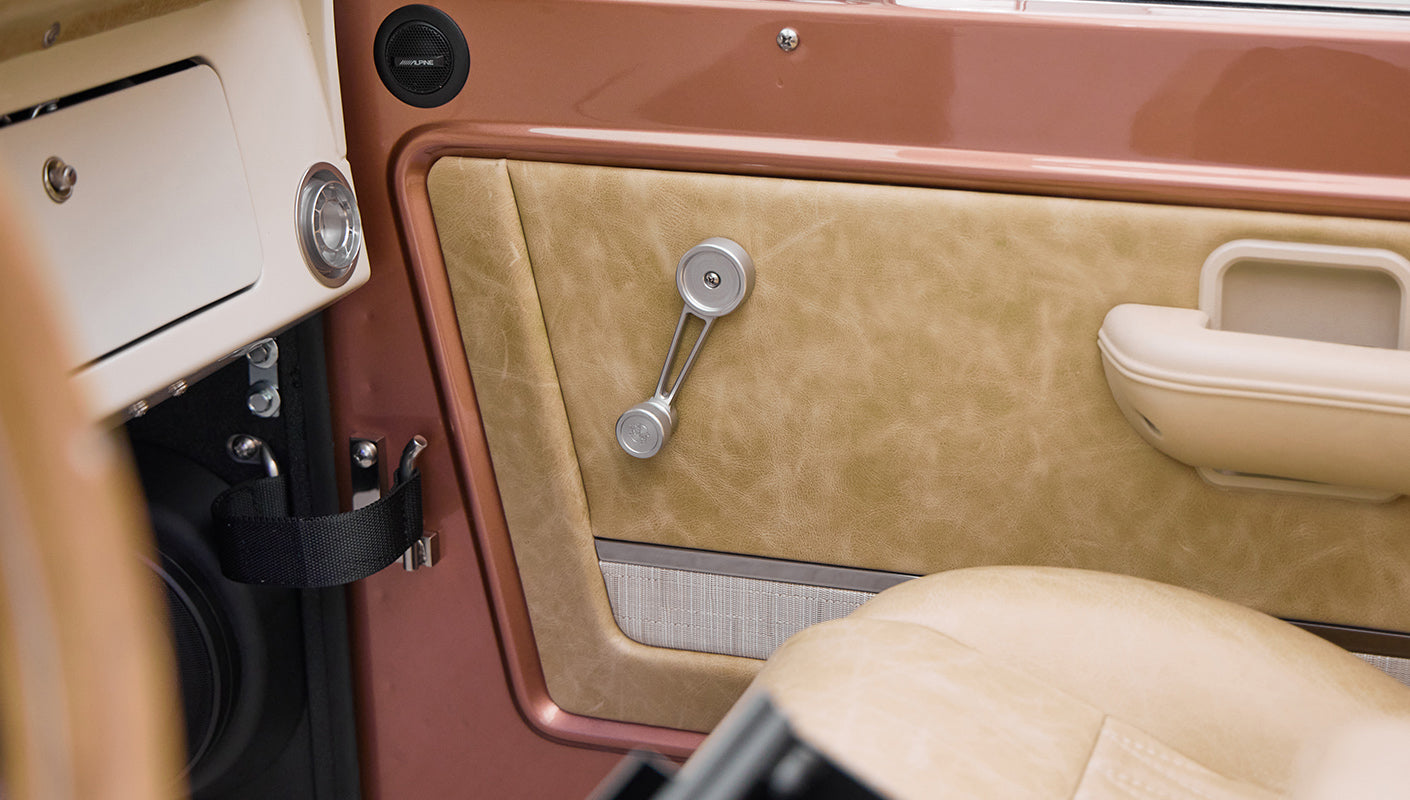 Interior door panel with beige and brown upholstery and manual window crank in Classic Ford Bronco