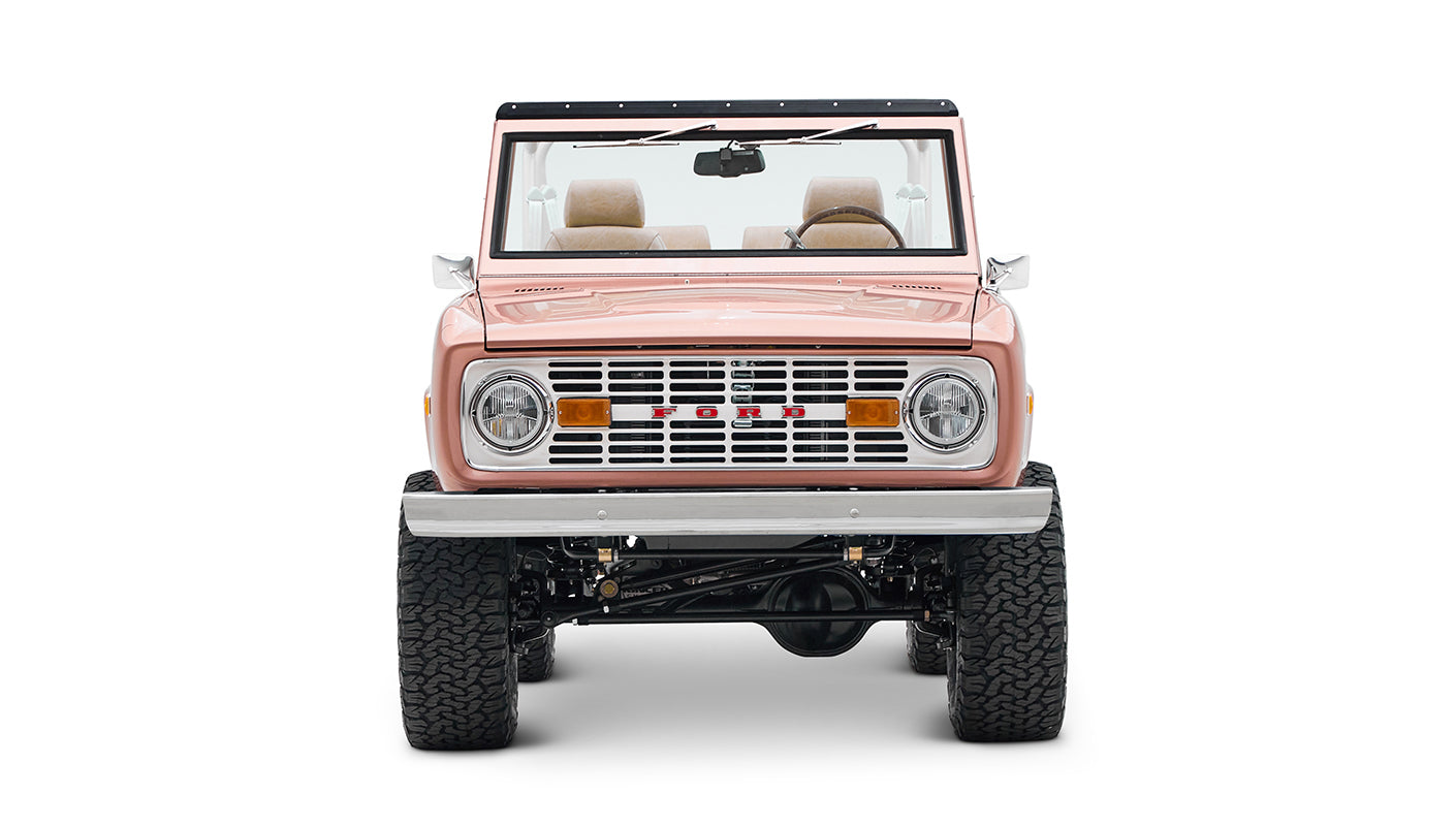 Classic Ford Bronco in pinkish paloma color with white roll cage, front view on white background
