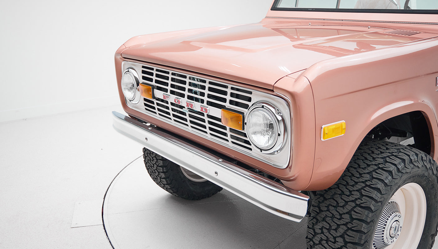 Front section of a Classic Ford Bronco with pinkish exterior and chrome bumper