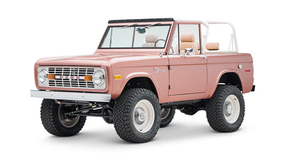 Classic Ford Bronco in pinkish paloma color with white roll cage, front three-quarter view on white background