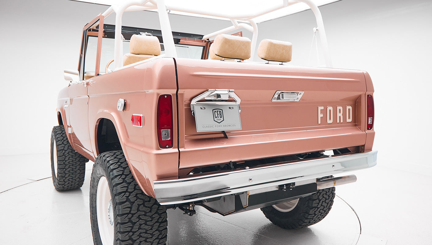 Rear view of a bronze Classic Ford Bronco showing the tailgate, bumper, and roll cage