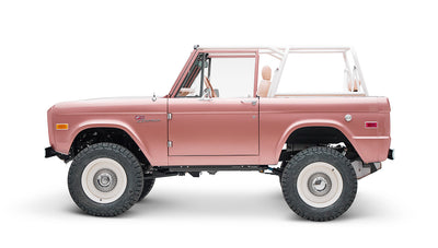 Classic Ford Bronco in pinkish paloma color with white roll cage, side profile on white background