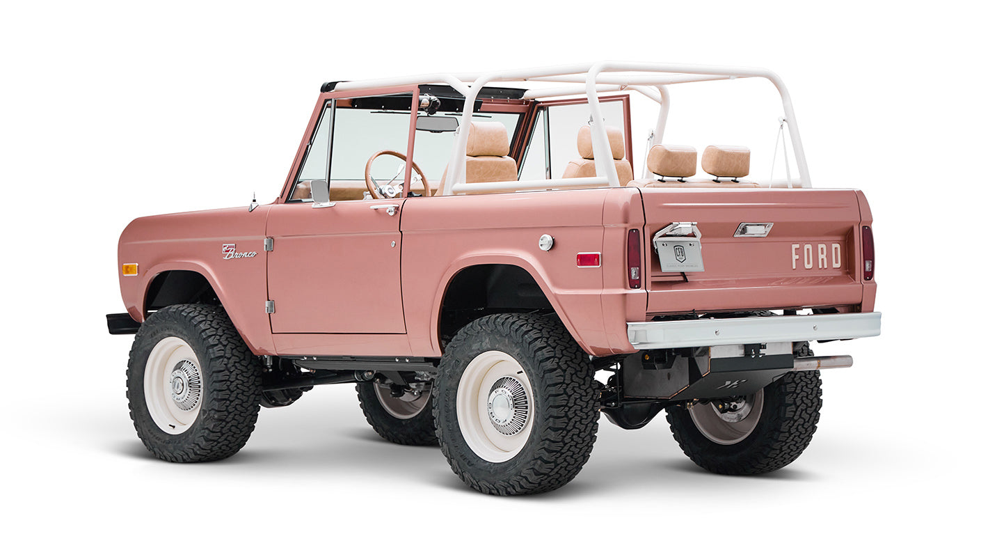Classic Ford Bronco in pinkish paloma color with white roll cage, rear side view on white background