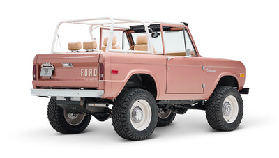 Classic Ford Bronco in pinkish paloma color with white roll cage, rear side view on white background