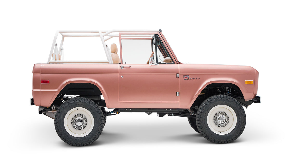 Classic Ford Bronco in pinkish paloma color with white roll cage, side profile on white background