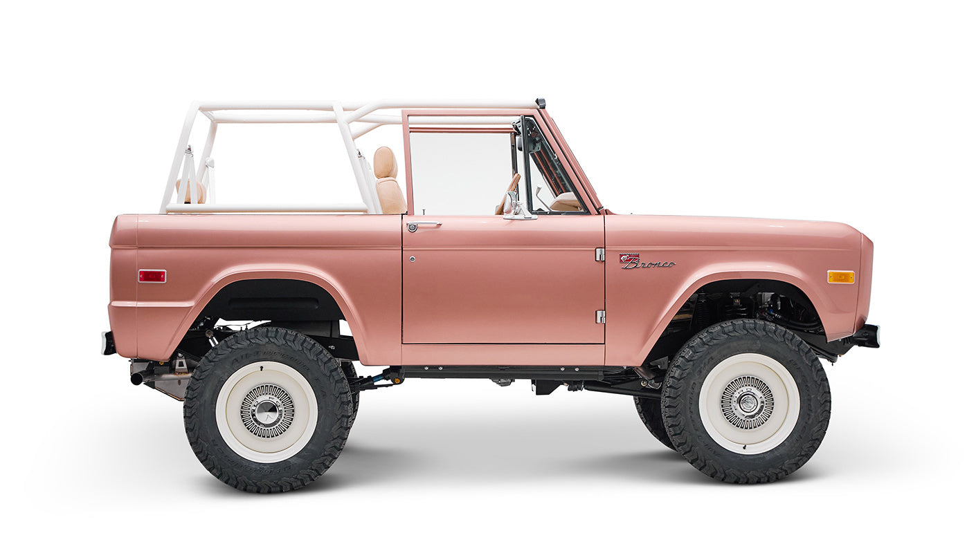 Classic Ford Bronco in pinkish paloma color with white roll cage, side profile on white background