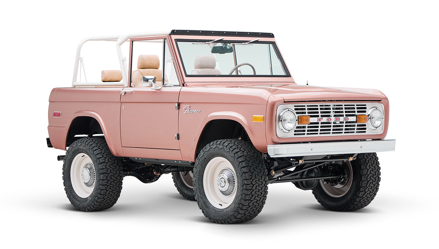 Classic Ford Bronco in pinkish paloma color with white roll cage, front three-quarter view on white background