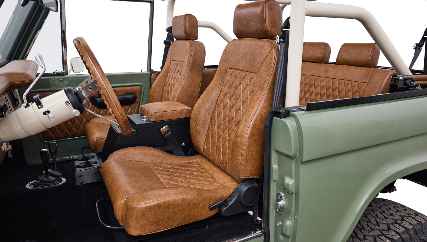 Interior view of Classic Ford Bronco showing brown seats, steering wheel, and roll cage.