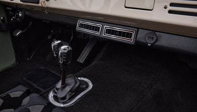 Two black gear shift levers and floor pedals on black carpet inside Classic Ford Bronco