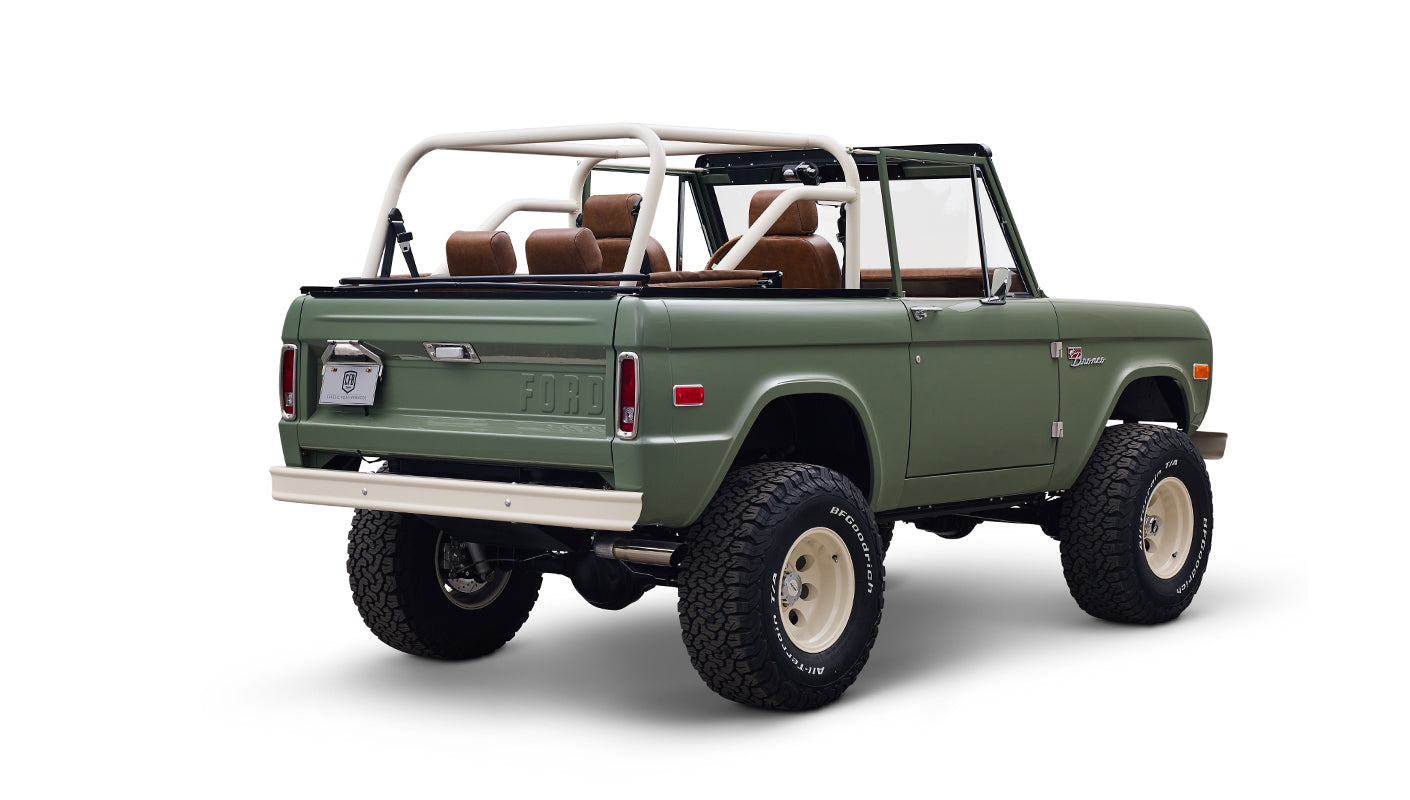 Angled rear view of green Classic Ford Bronco with tall off-road tires and white wheels