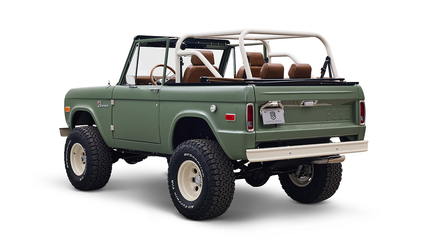 Rear view of green Classic Ford Bronco with white wheels, shown on white background