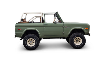 Side profile of green Classic Ford Bronco with open top and tan leather seats on white background