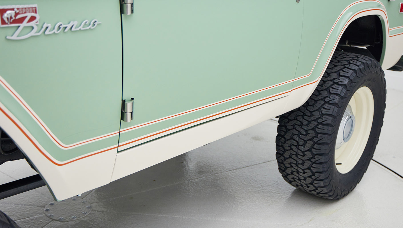 Side view of porcelain green classic Ford Bronco showcasing door, fender, and tire with white and orange trim