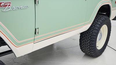 Side view of porcelain green classic Ford Bronco showcasing door, fender, and tire with white and orange trim